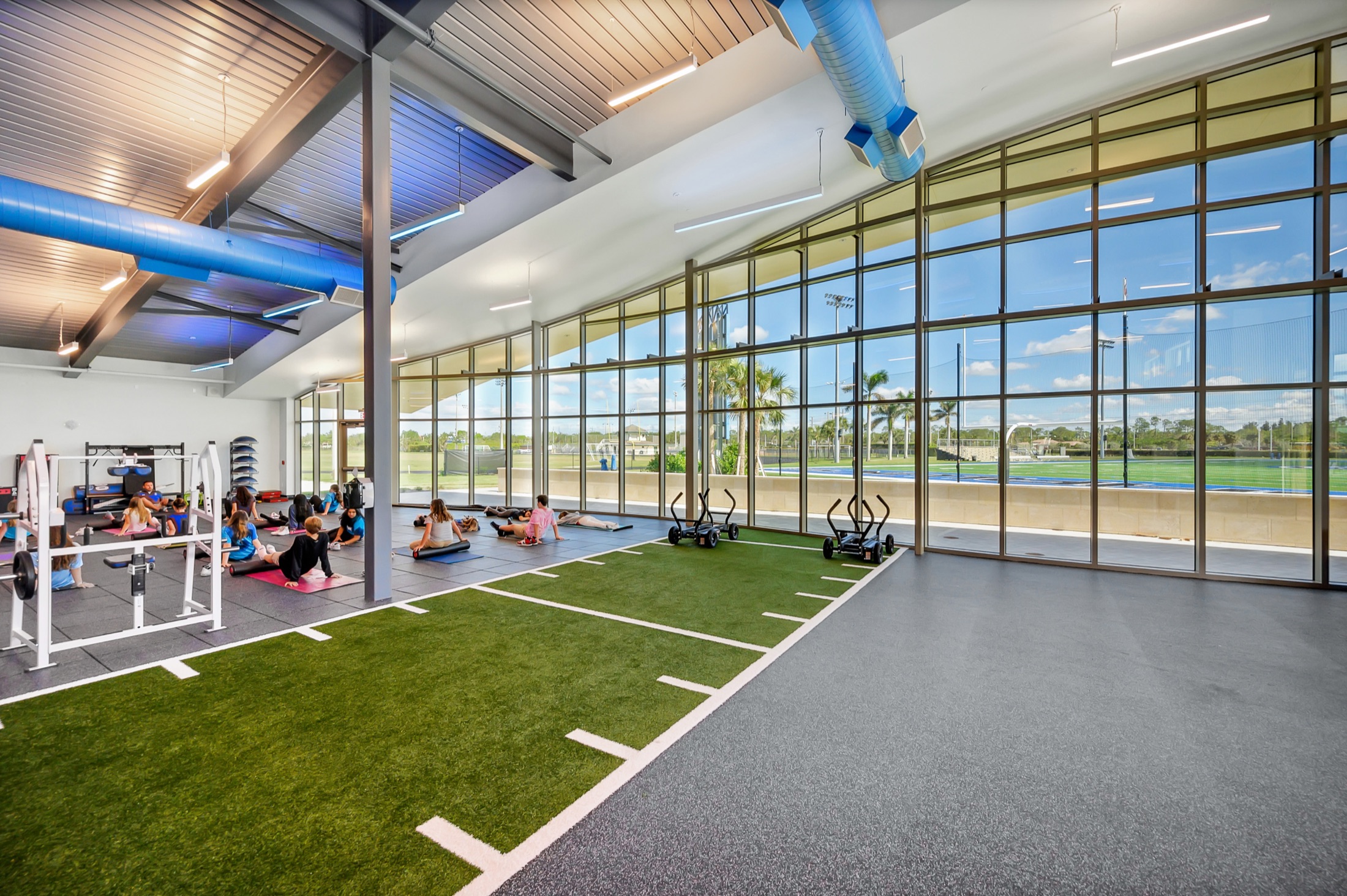 Athletes stretching on indoor training turf beside floor-to-ceiling windows